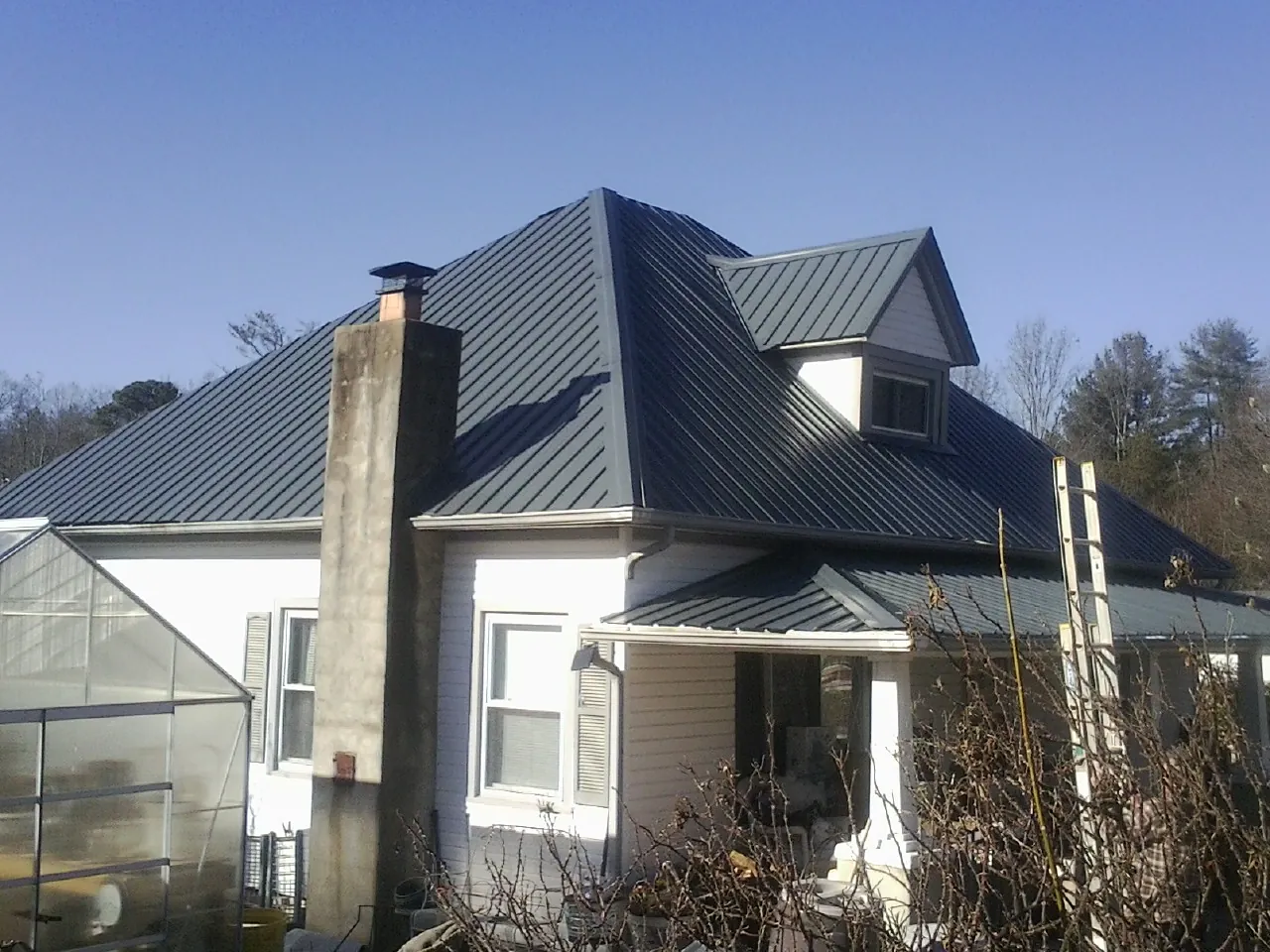 Dark blue standing seam metal roof on a white farmhouse with dormer — Slate & Tile Roof Repair by Roofing Brothers in Kathryn