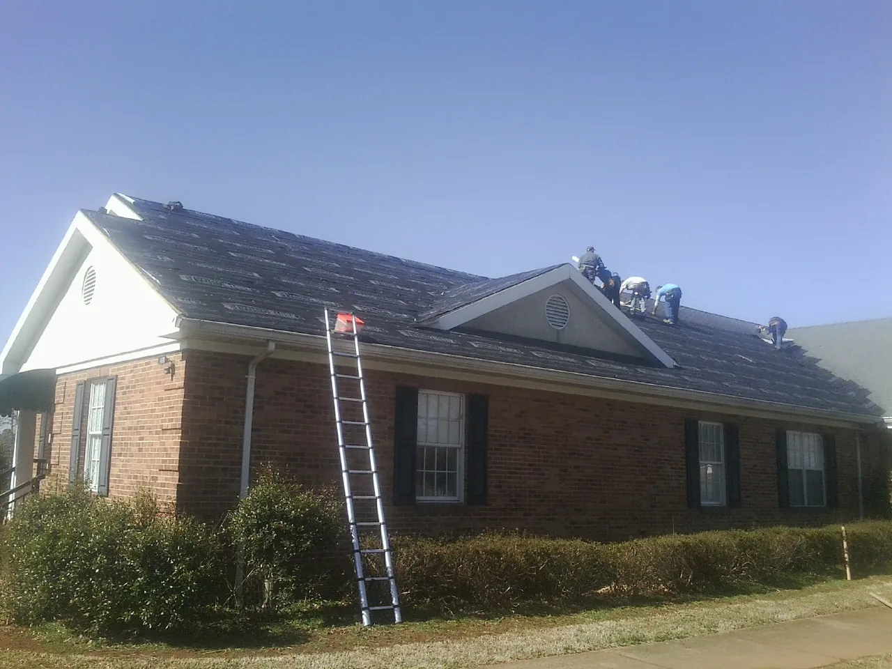 Crew tearing shingles off a brick ranch roof with a ladder set — Emergency Roof Repair work by our crew in Kathryn