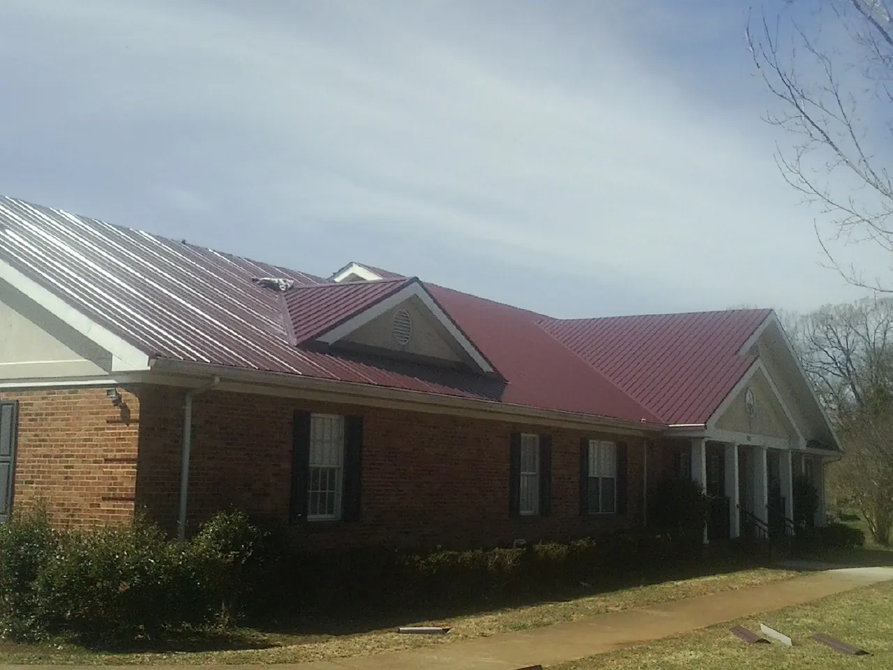 Red metal roof with gabled entries on a long brick building, from a Hail Damage Roof Repair job in Kathryn