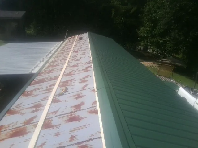 Old rusted panels beside newly installed green metal roofing — Wind Damage Roof Repair by Roofing Brothers in Kathryn