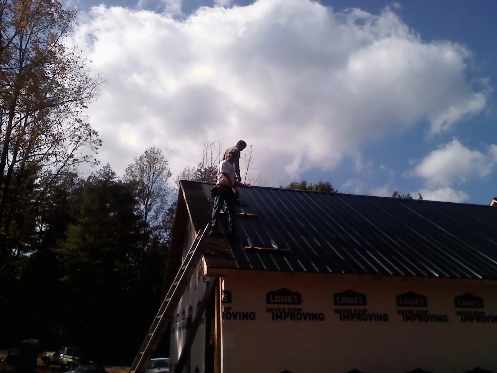 Roofer fastening dark metal panels high against a cloudy sky, from a Roof Inspection job in Kathryn