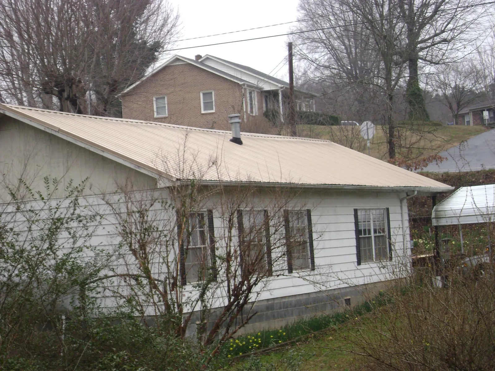 Tan metal roof on a white sided house set into a hillside — Commercial Roofing by Roofing Brothers in Kathryn